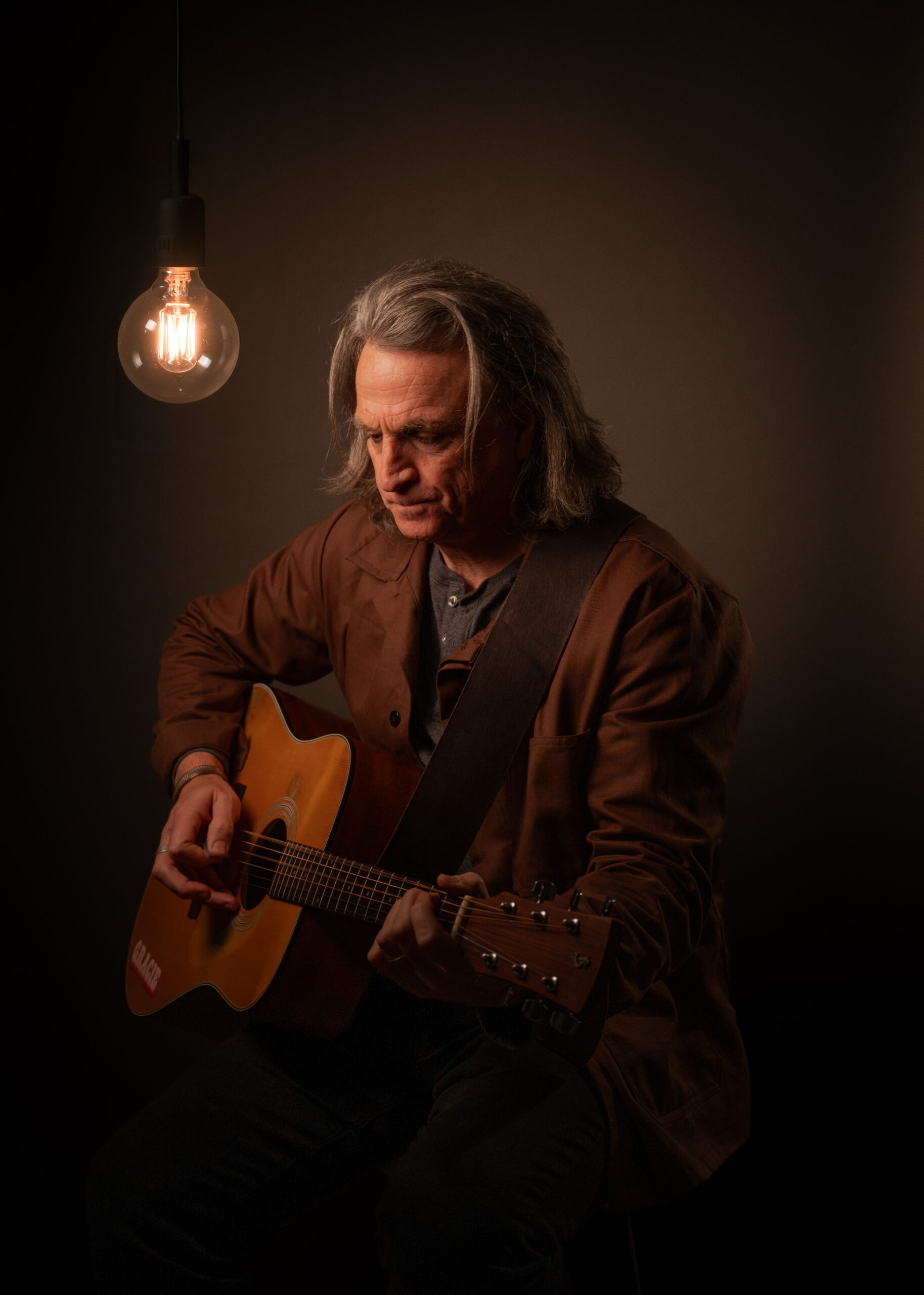 Fender Jones playing acoustic guitar beside a glowing studio bulb